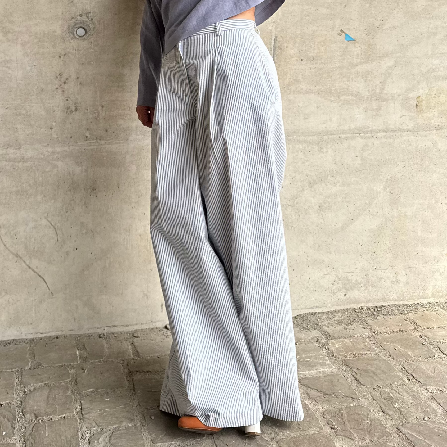 Woman in striped  pants standing against a concrete wall.