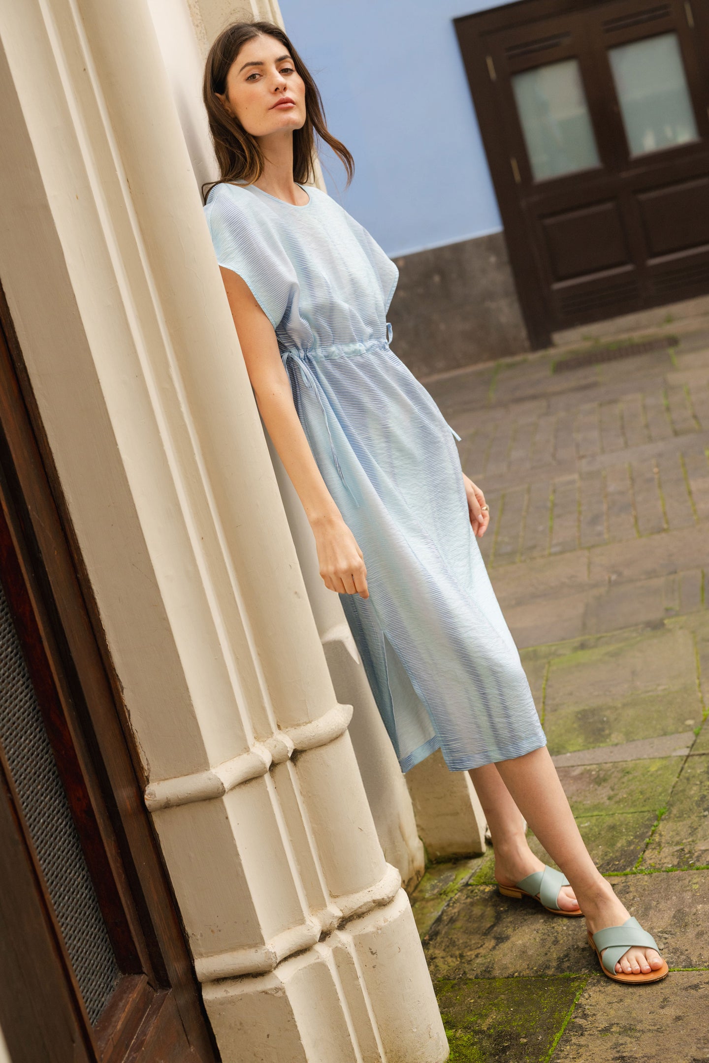 Woman in a light blue dress standing outside a building with a stone floor.