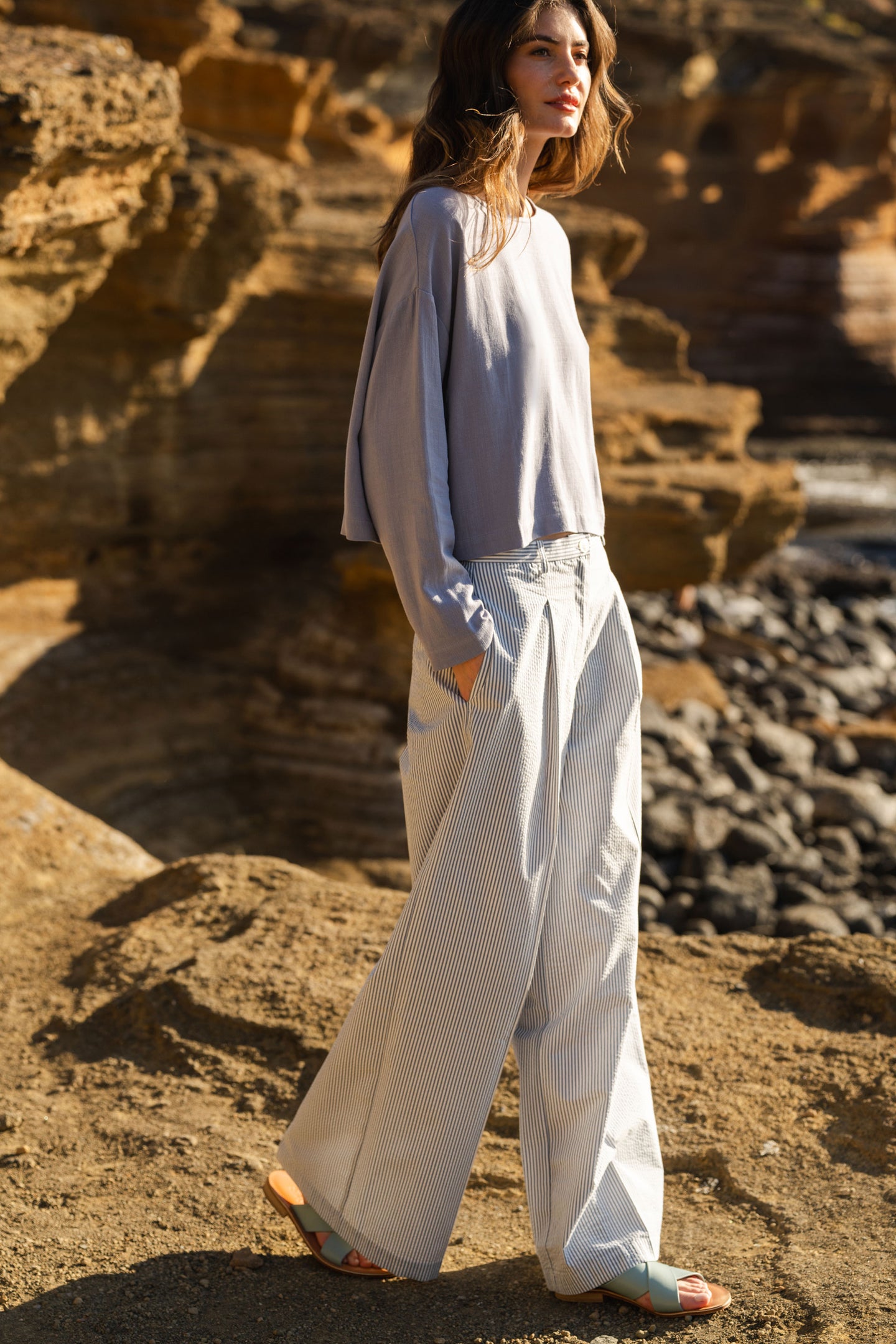 Woman in a blue stone blouse and striped seersucker pants standing on rocky terrain