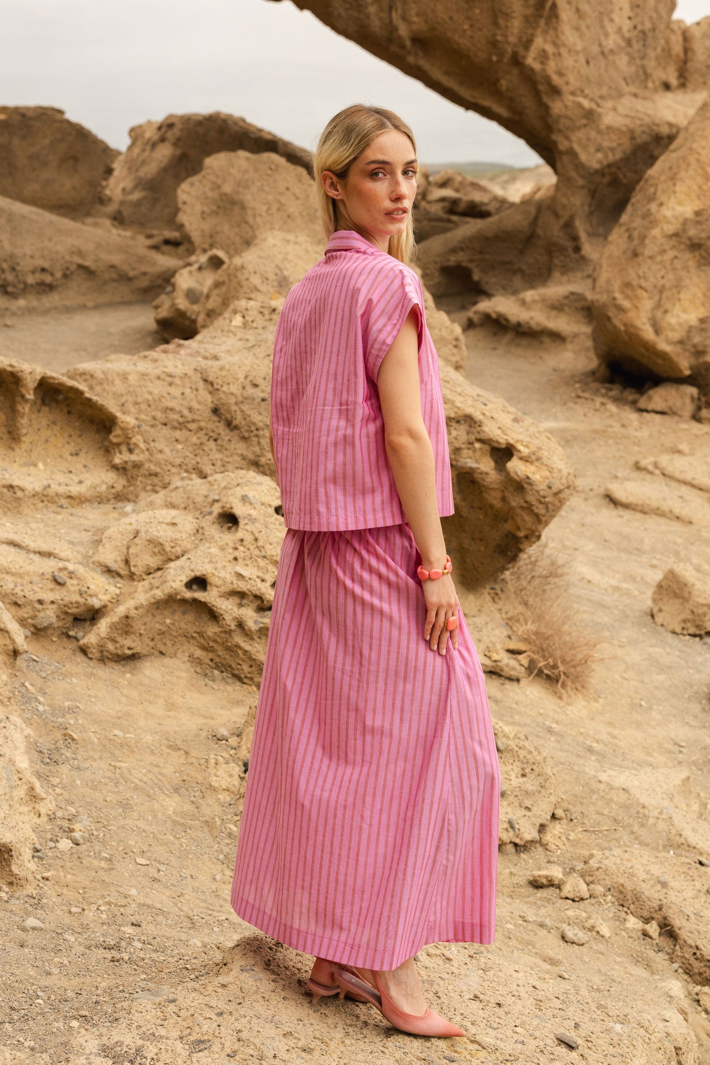Woman in a pink striped outfit standing in a rocky desert landscape