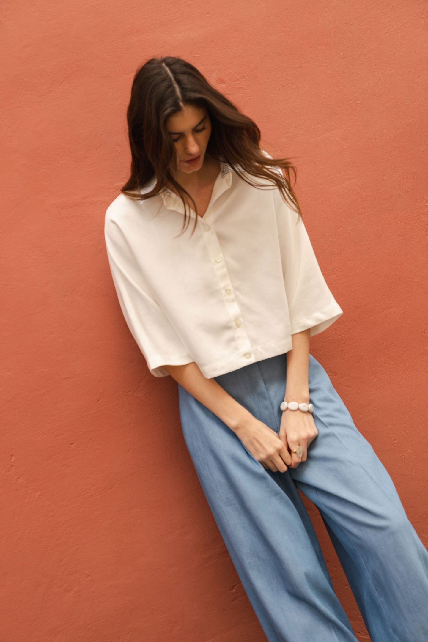 Woman wearing a white blouse and blue jeans pants against a red-brown wall