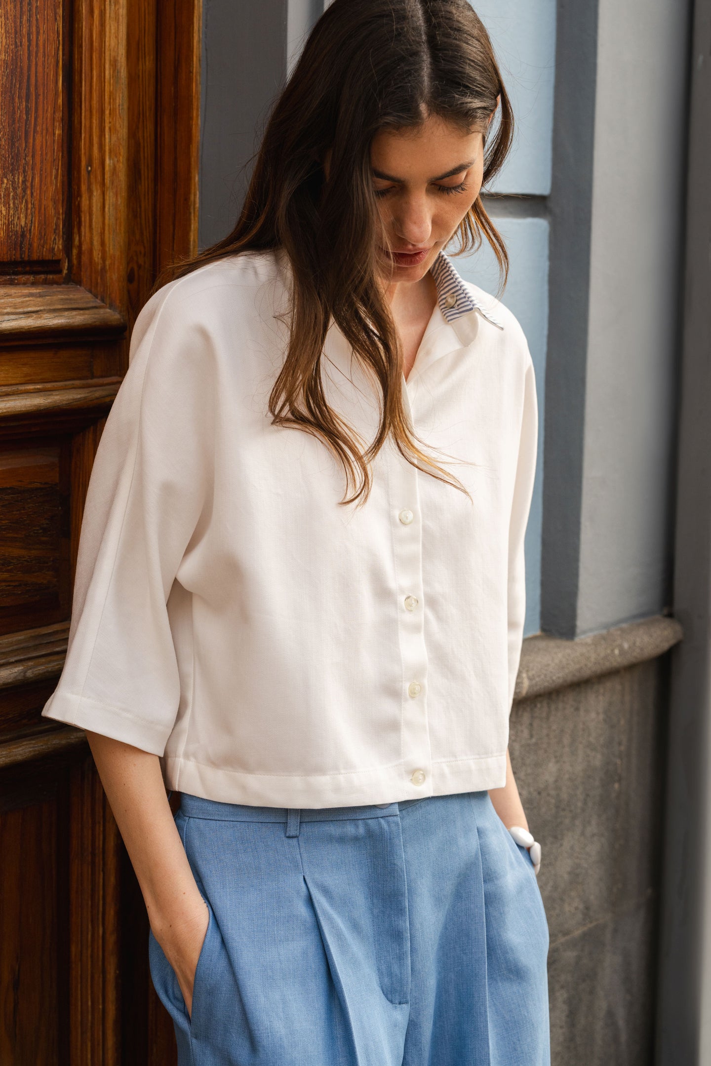 Woman wearing a white blouse and blue pants standing indoors.
