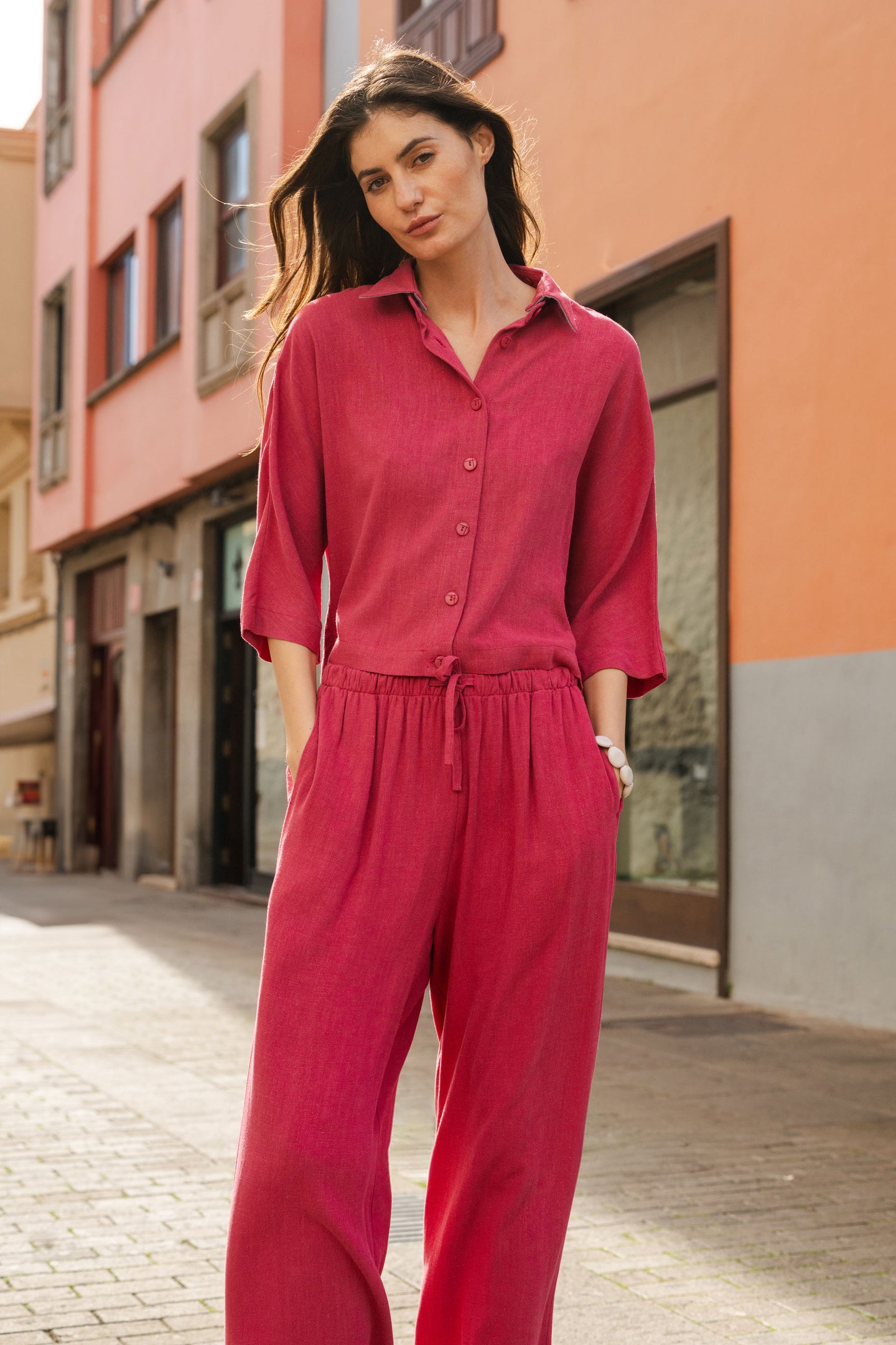 Woman wearing a magenta outfit standing on a street with colorful buildings.