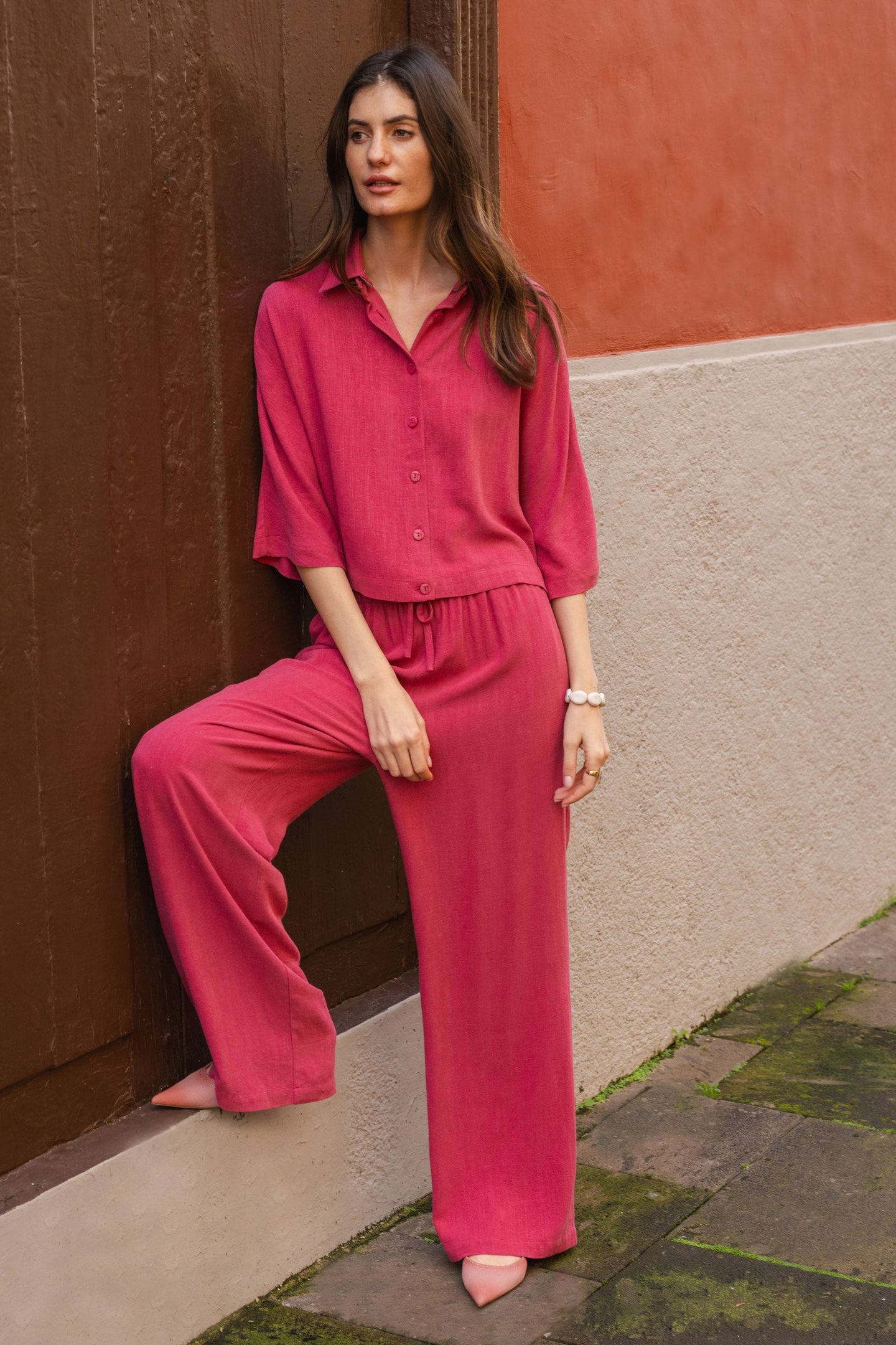 Woman in a magenta outfit standing against a wall with a textured surface.