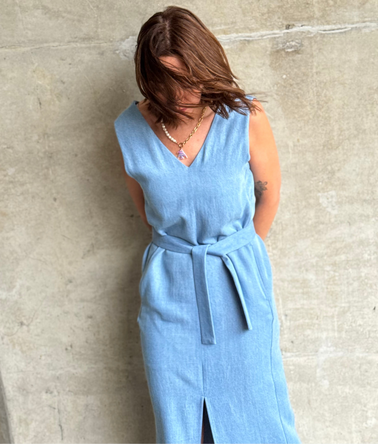 Woman wearing a light blue jeans dress against a concrete wall.