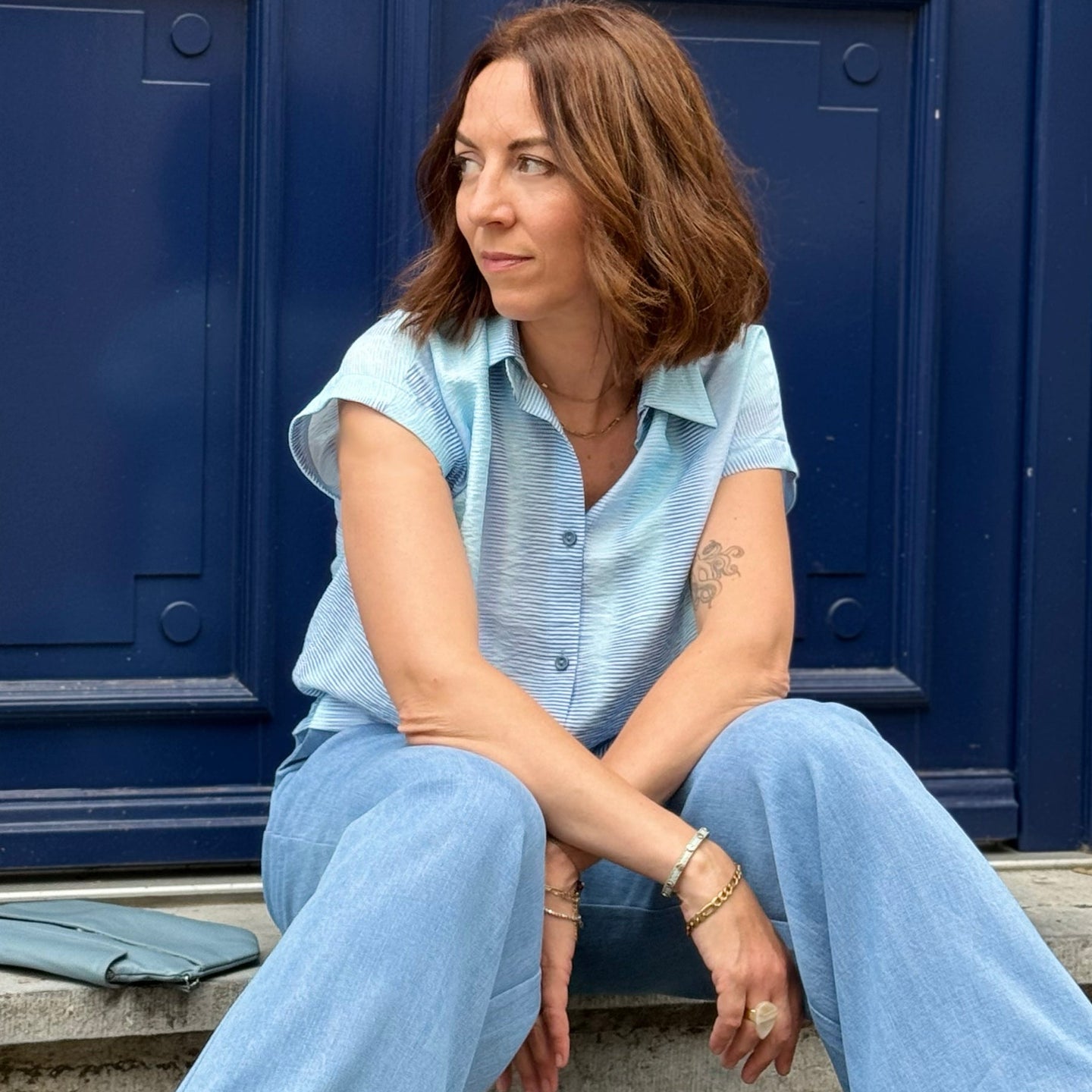 Woman in a light blue blouse & jeans sitting against a blue background
