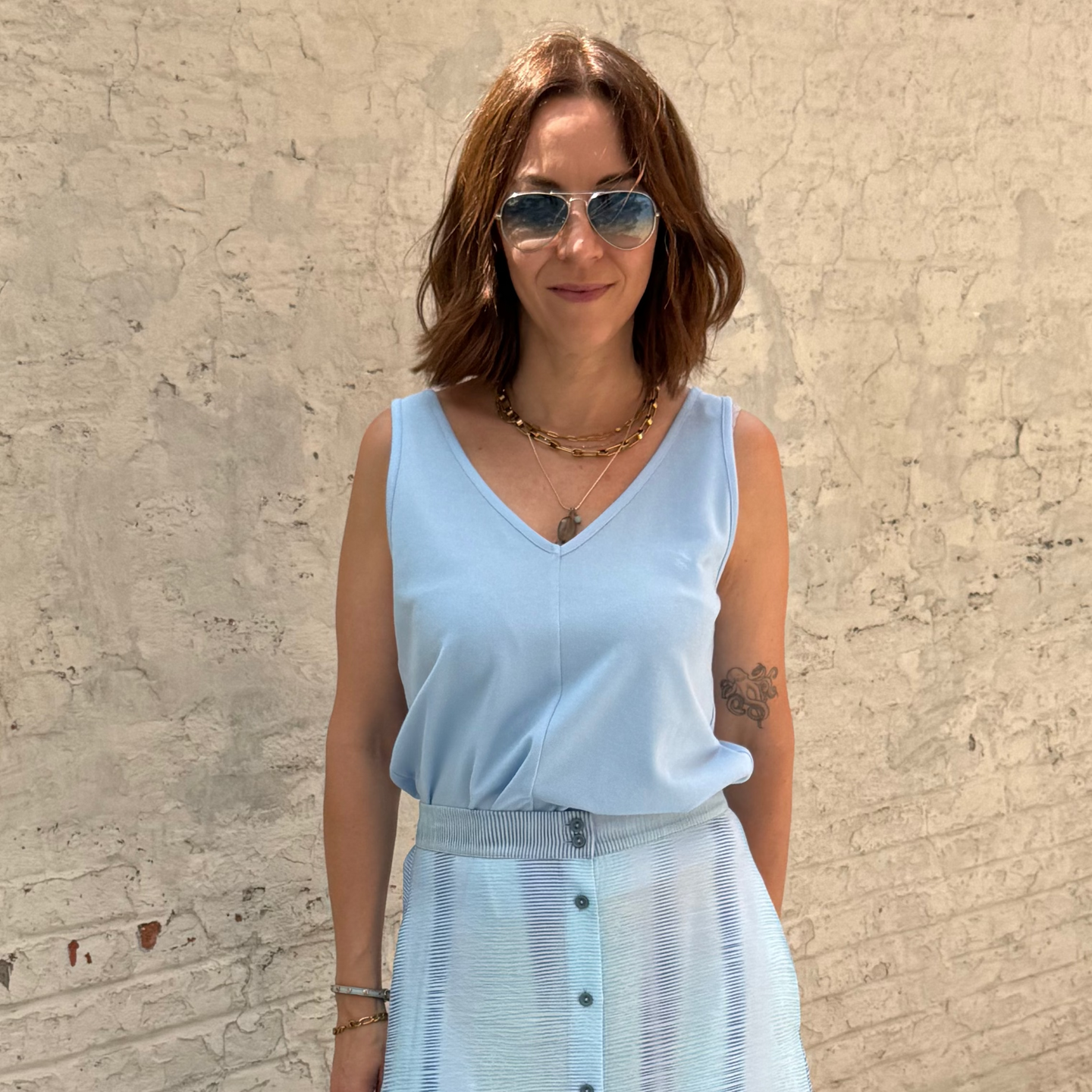 Woman wearing a light blue sleeveless top and skirt against a textured beige wall.