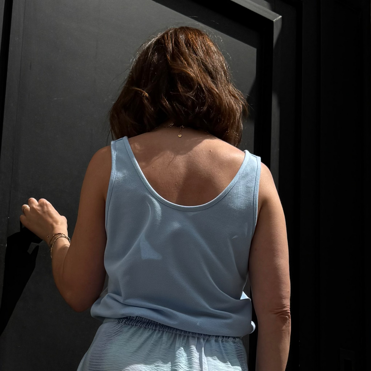 Person wearing a light blue sleeveless top, standing in front of a dark background.