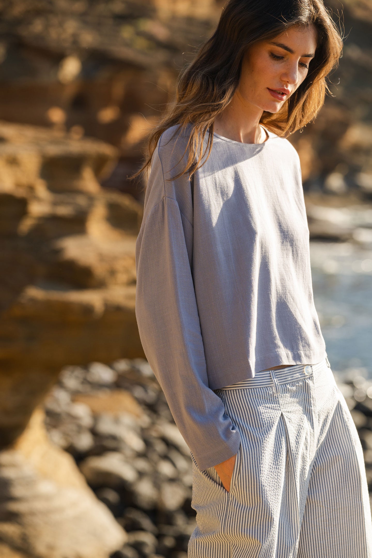 Woman in a blue stone blouse standing against a natural rock background