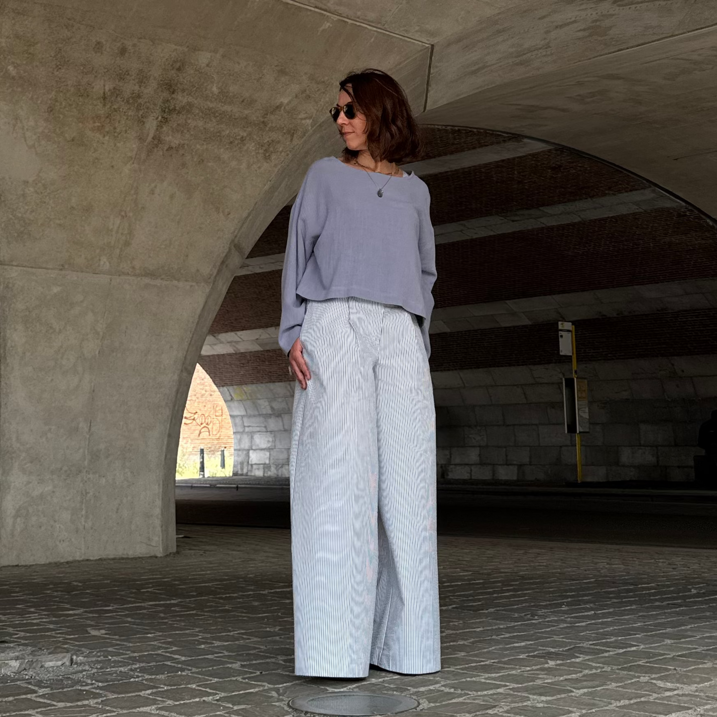 Woman in striped pants and blue top standing in a concrete archway with a textured floor